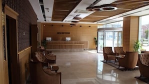 A reception area with a wooden reception desk, several leather armchairs, and a large window providing natural light. - YZE Pirlanta Hotel (Malatya)