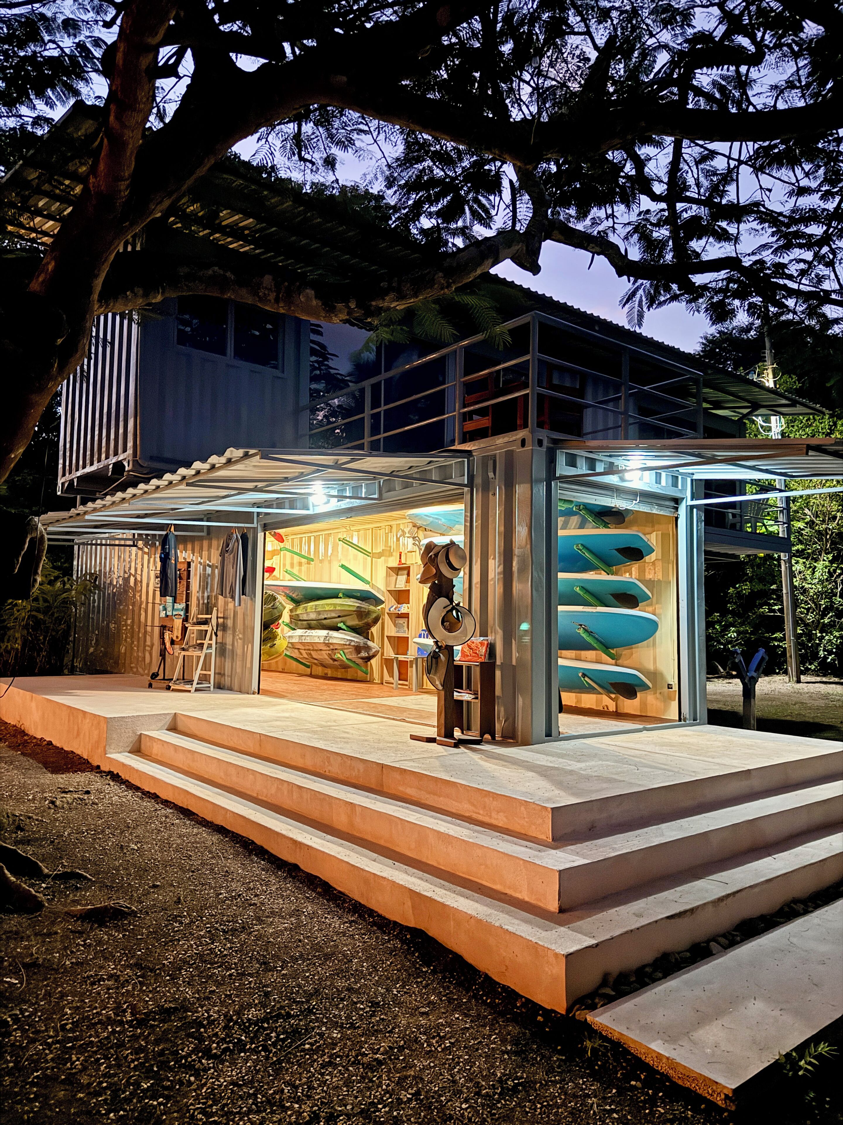 Een modern gebouw met een glazen gevel, een terras en een etalage met surfplanken.