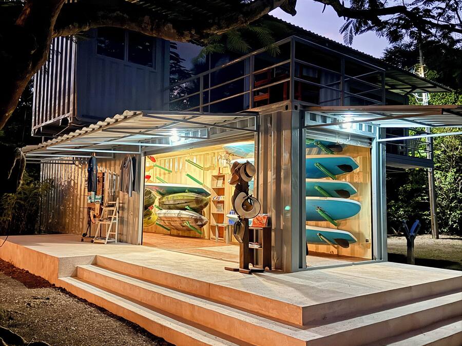 Een modern gebouw met een glazen gevel, een terras en een etalage met surfplanken.