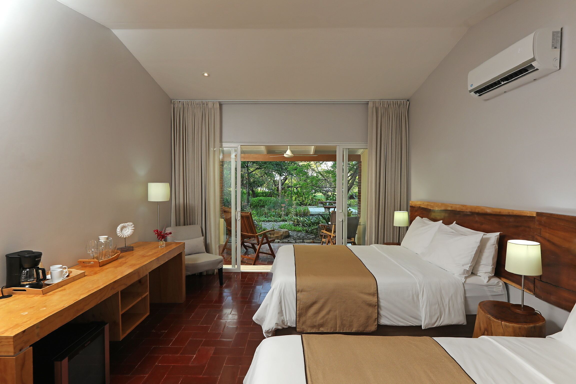 A hotel room with a bed, bedside tables, a desk with a coffee maker, and a view of the outdoors through a sliding door.