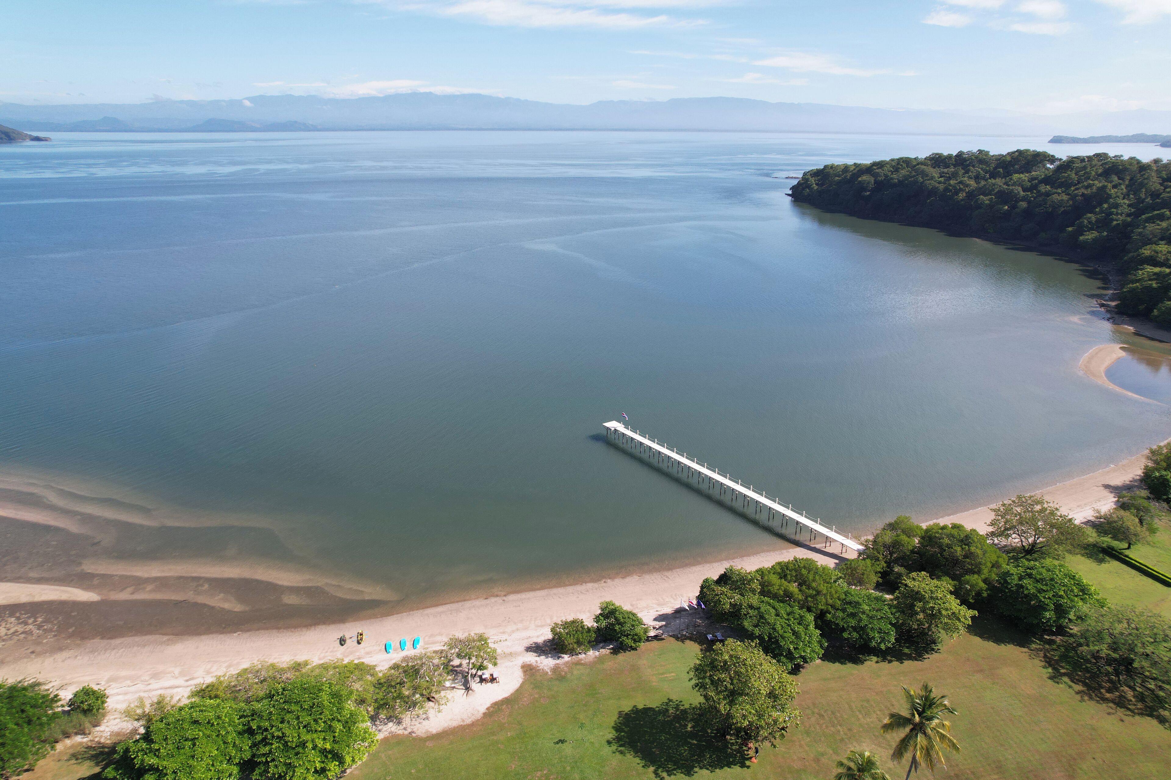 Vista aérea de una zona costera con un puente, playa y terreno boscoso.