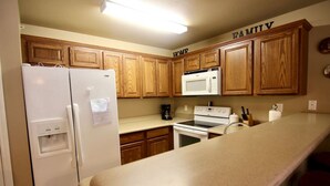 Una cocina con armarios de madera, un refrigerador blanco, microondas, horno y encimera.