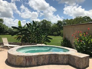 Uma banheira de hidromassagem com exterior de pedra, rodeada por vegetação e uma parede de tijolos.