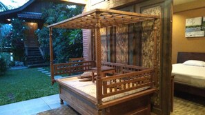 A wooden four-poster bed with a mattress and pillows, positioned in a room with a bed and a painting on the wall. - Jatiwangi Villa (Penebel)