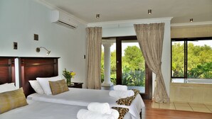 Une chambre d’hôtel avec deux lits, une grande fenêtre avec des rideaux, une vue sur la verdure et un climatiseur fixé au mur.