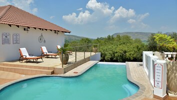 Zona de piscina con sillones de descanso, un edificio junto a la piscina y vistas del paisaje circundante.