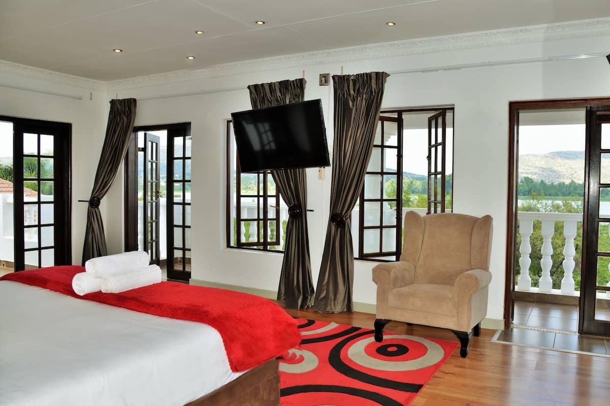Een hotelkamer met een groot bed, een televisie, een stoel en een balkon met uitzicht op de omgeving.