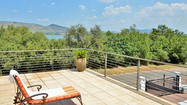 Un balcon avec vue sur un lac et des montagnes, une plante en pot et un fauteuil de relaxation.