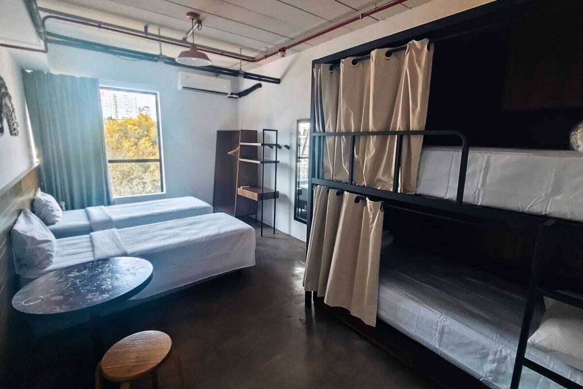 Un dormitorio con literas, una mesita, una silla y una ventana con cortinas.