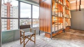 Una habitación de hotel moderna con un ventanal grande, un banco de madera y una estructura de cama de metal con cortinas.