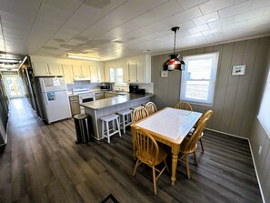 A kitchen with wooden flooring, a dining table with chairs, and a hanging light fixture.
