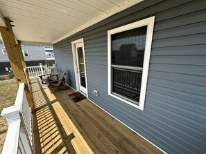 A covered porch with a wooden deck, a white railing, and a door leading to a garage.