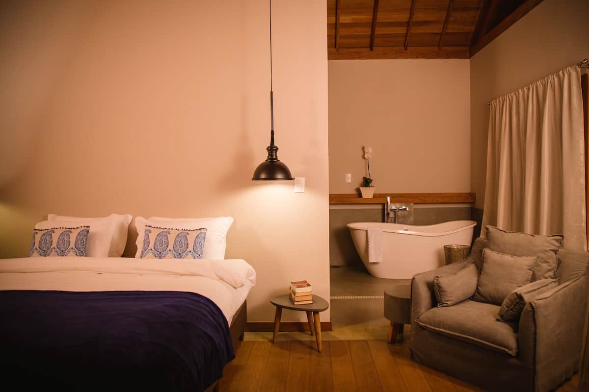 Ein Schlafzimmer mit Bett, Nachttisch, Lampe und einem Sessel.