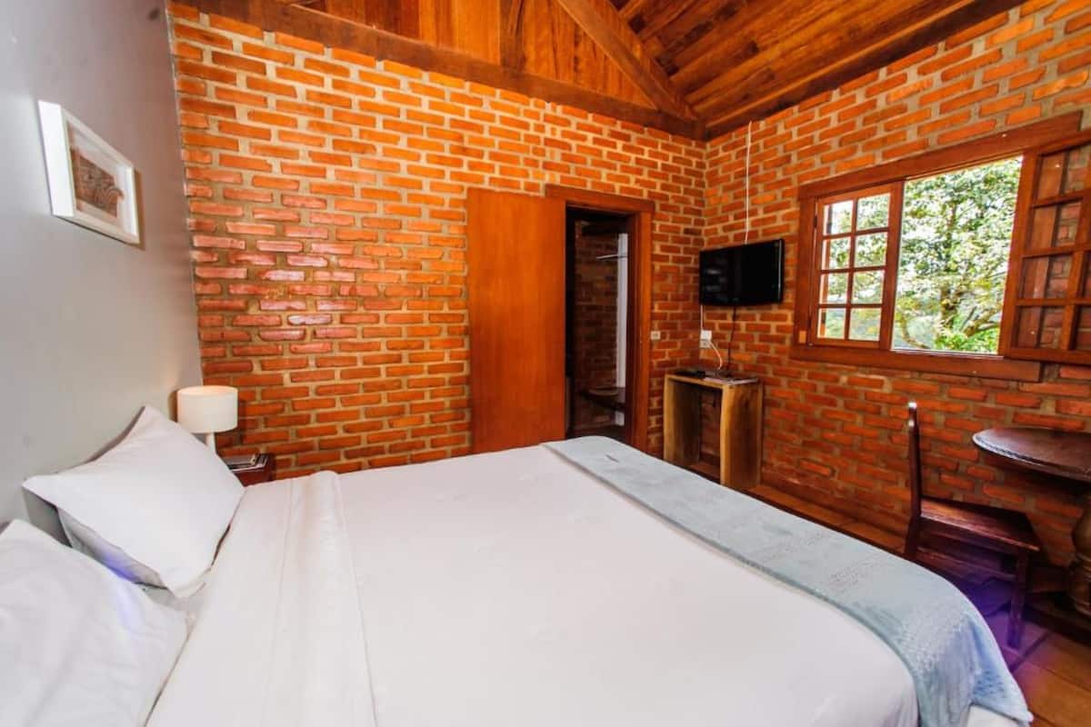 Ein Zimmer mit Backsteinwand, einem Bett, einem Fernseher, einem Fenster und einem kleinen Tisch.