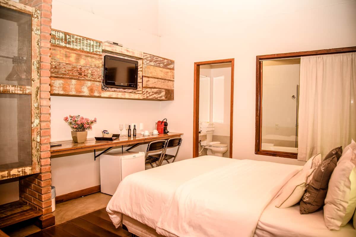 Ein Schlafzimmer mit Bett, Schreibtisch mit Fernseher, kleinem Kühlschrank und angrenzendem Badezimmer.