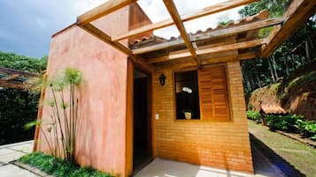 Un petit bâtiment en briques, doté d’une entrée surmontée d’une pergola en bois, et entouré de verdure.