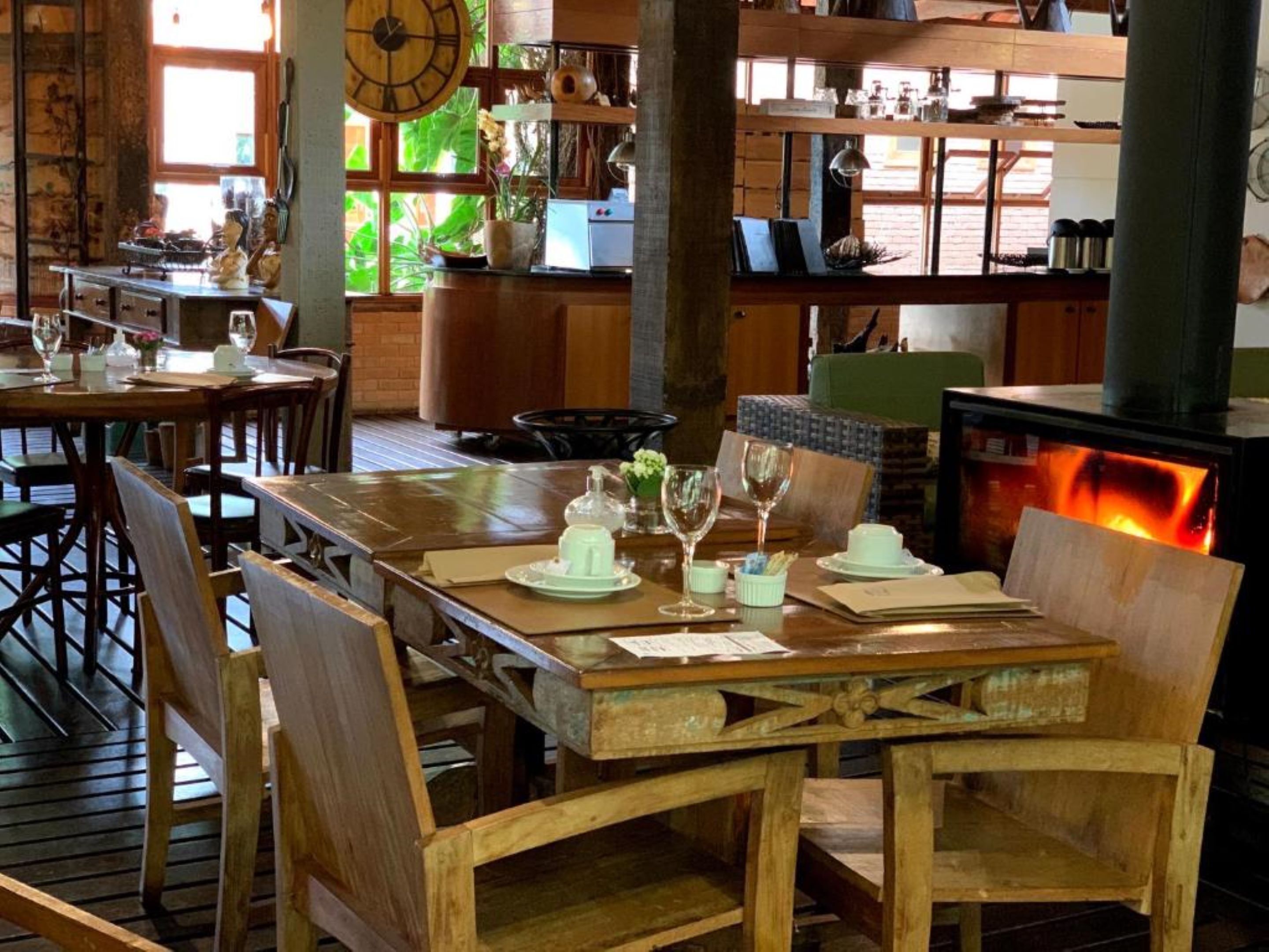 Un comedor rústico con mesas y sillas de madera, una chimenea y estantes con utensilios de cocina.
