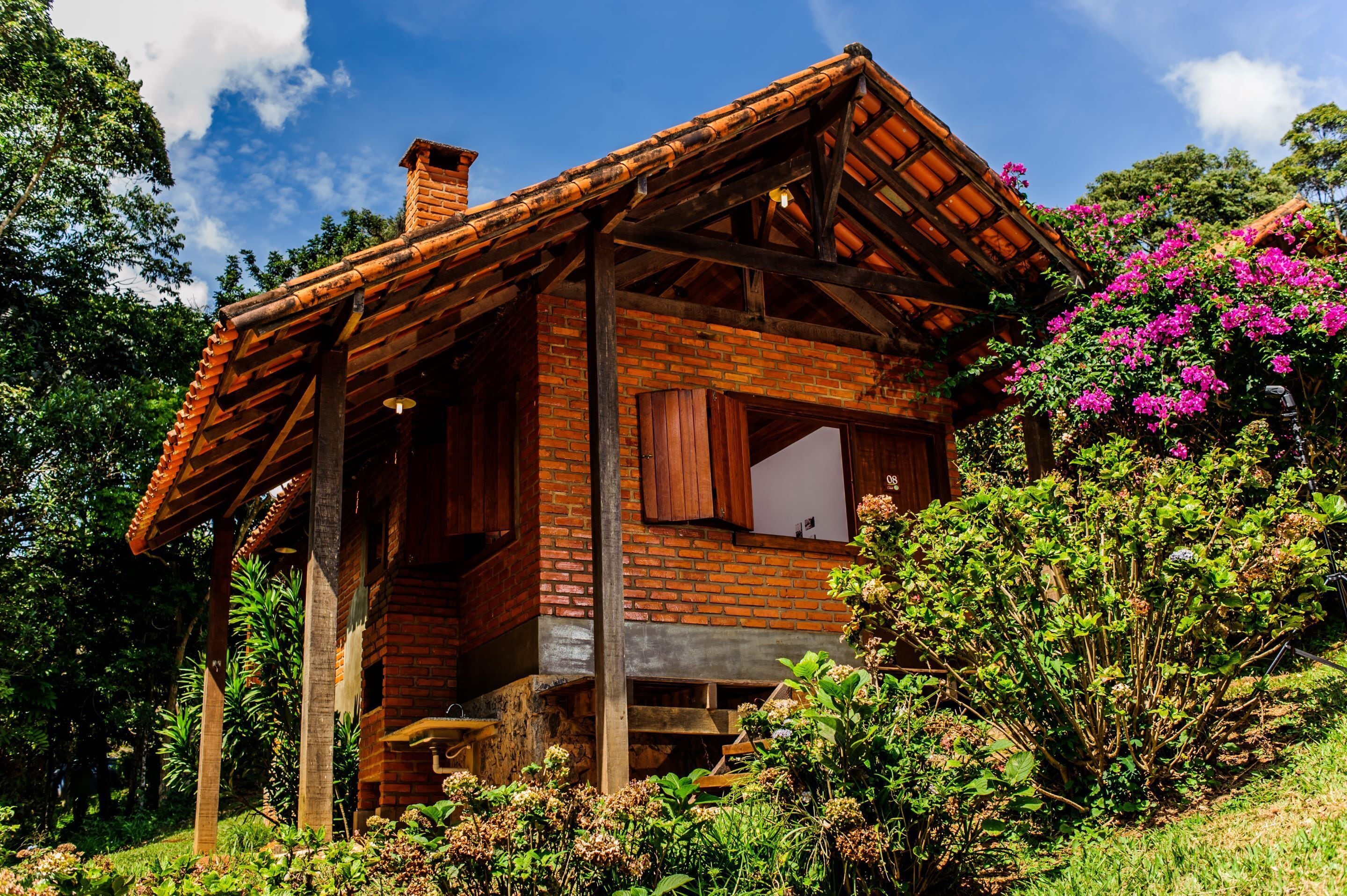 Eine rustikale Holzhütte mit geneigtem Dach, umgeben von üppigem Grün und blühenden Pflanzen.