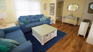 Uma sala de estar com um sofá azul, uma mesa de centro branca e um tapete azul.