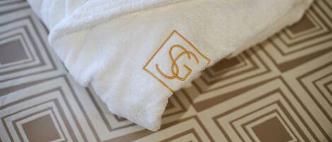 Una toalla blanca con un logotipo bordado en dorado sobre un suelo estampado.