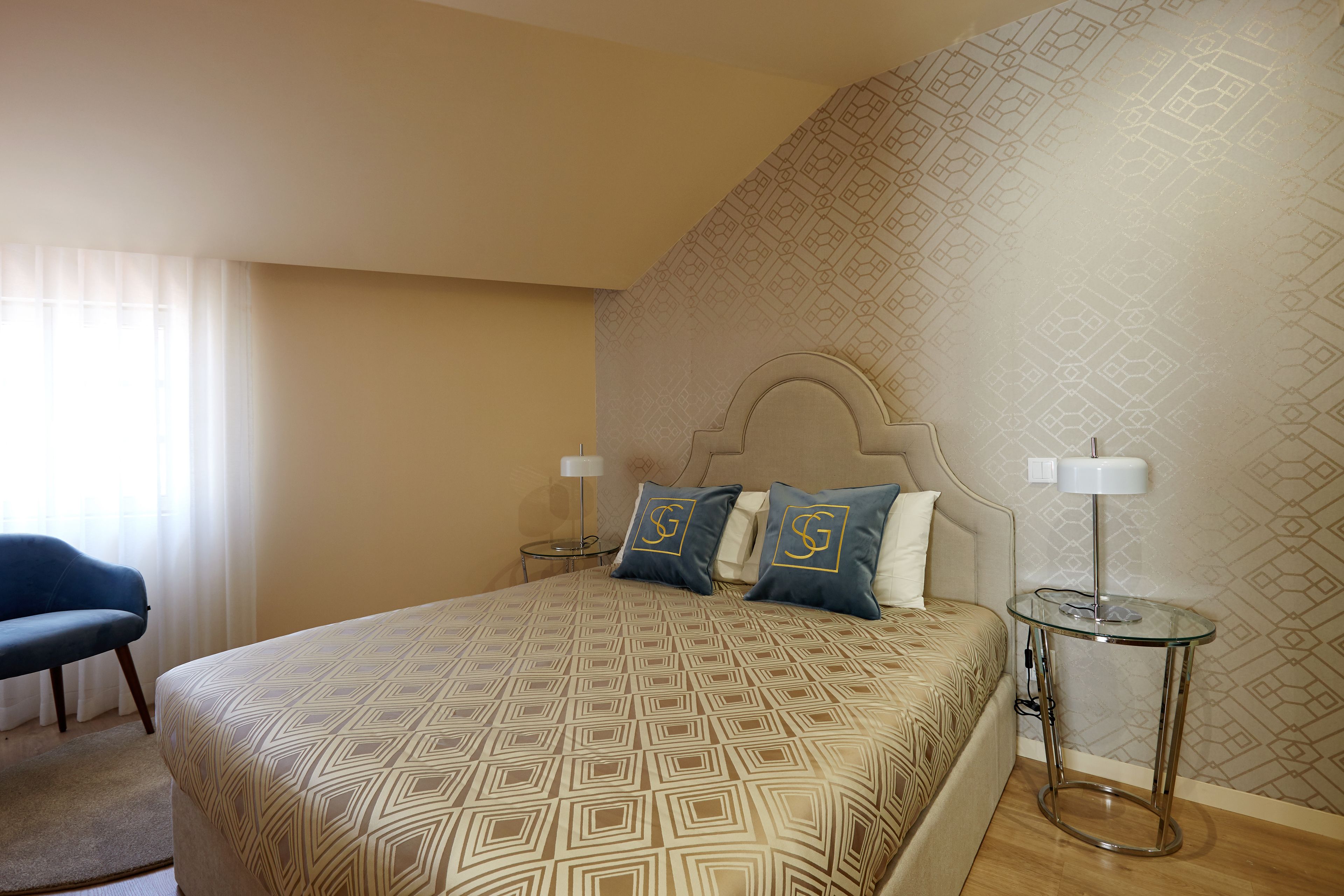 A hotel room with a large bed, two bedside lamps, a chair, and a patterned wall.