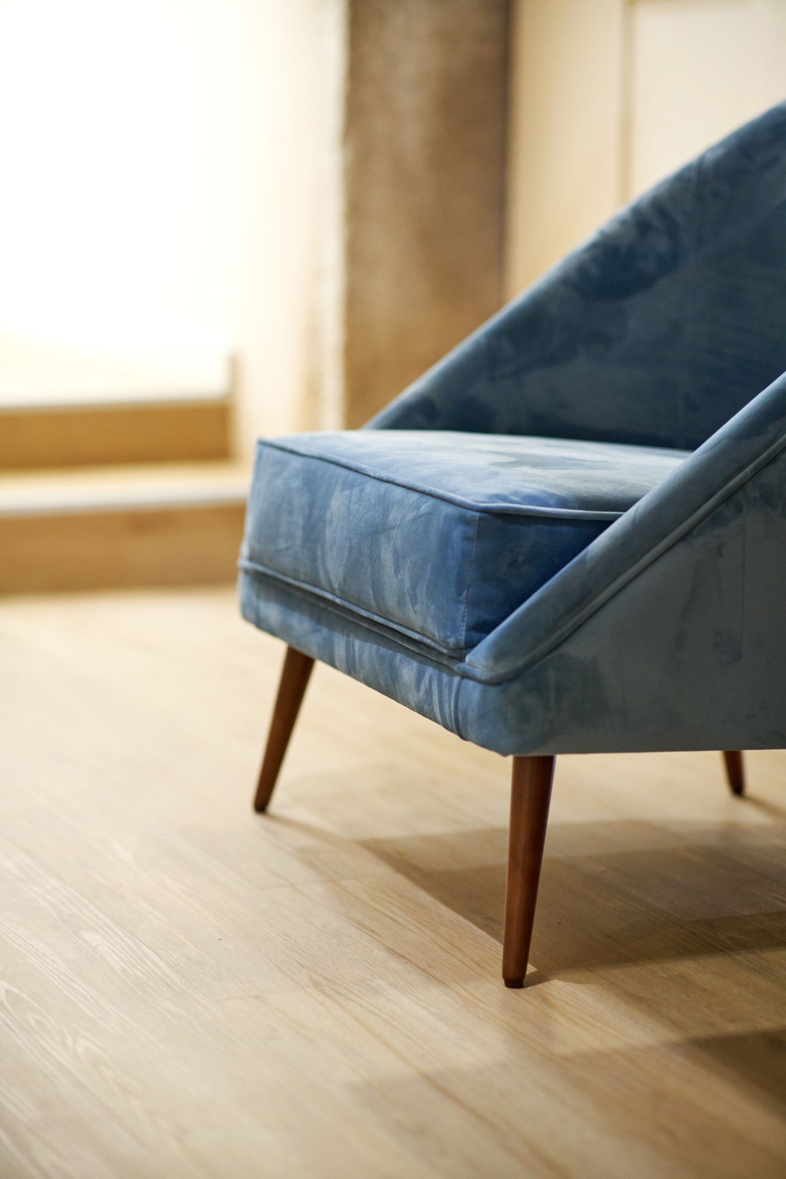 Ein blauer Sessel mit Holzbeinen auf Holzboden.