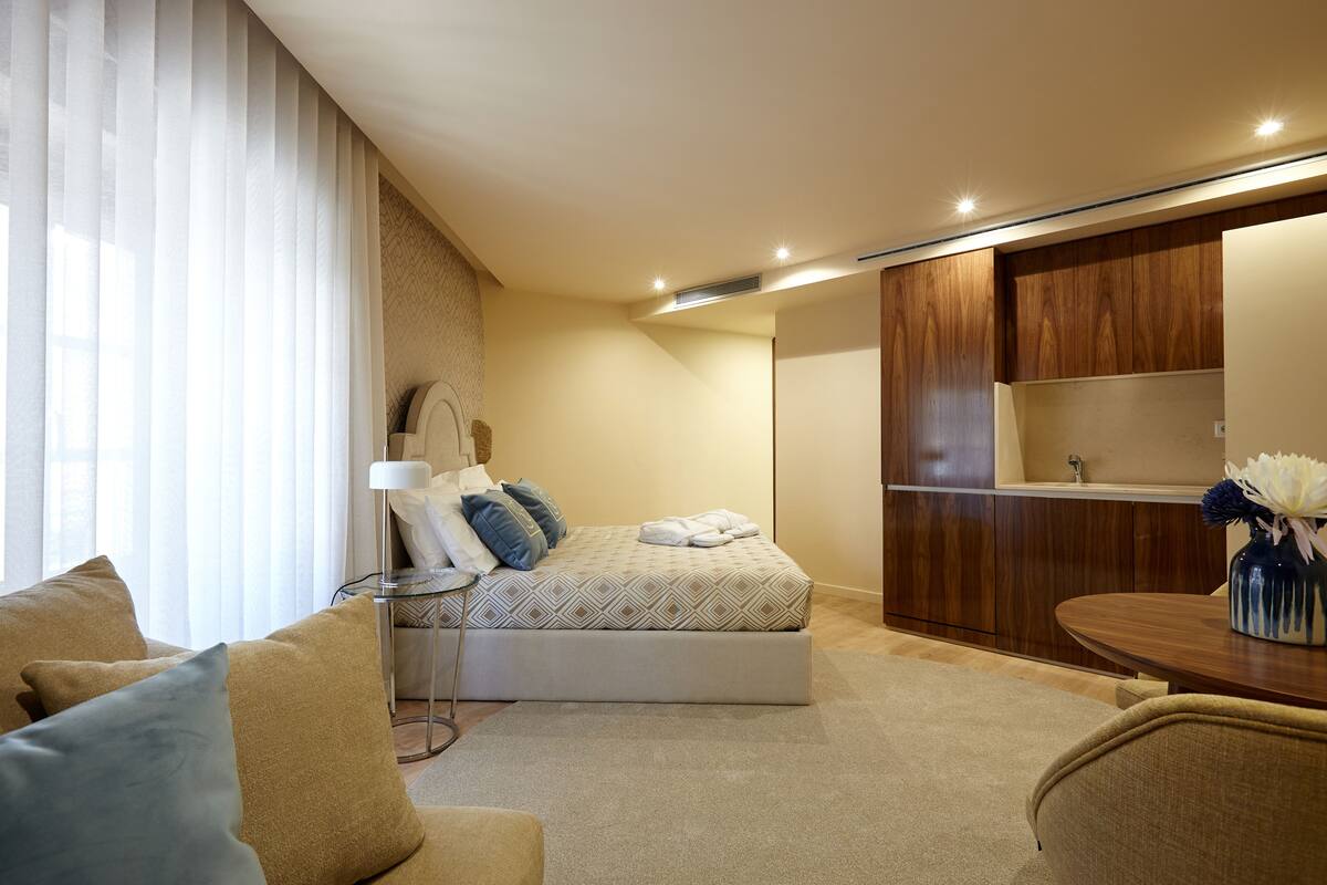Ein modernes Schlafzimmer mit Bett, Nachttisch, Lampe und einem kleinen Holzschrank.