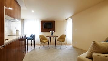 Un espacio habitable compacto con kitchenette, una zona de comedor con dos sillas, un sofá y un televisor de pantalla plana montado en la pared.
