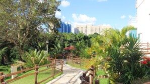 Un sendero serpentea por un exuberante jardín con vallas de madera, rodeado de follaje y palmeras.