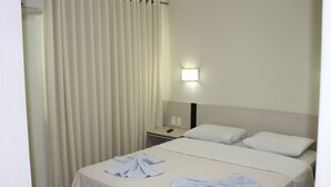 Una habitación de hotel con una cama, una mesita de noche, una lámpara y un ventanal con cortinas.