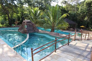 A swimming pool with a rock formation, surrounded by palm trees and a wooden deck. - Thermas do Bosque (Caldas Novas)
