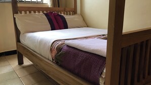 A single bed with a wooden frame, white bedding, and a purple blanket. - Capernaum Hotels (Kampala)