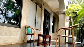 A balcony with two wooden chairs and a small table, a tiled floor, and a building entrance with a door and window. - Capernaum Hotels (Kampala)