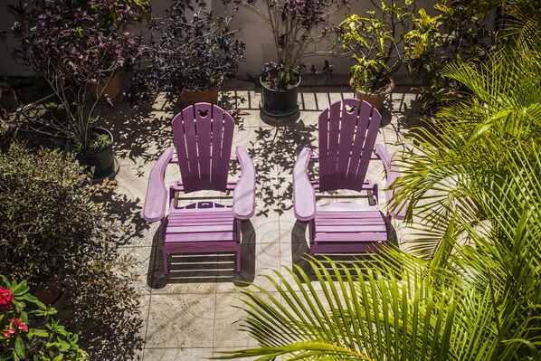 Two purple Adirondack chairs on a patio with potted plants and a tiled floor.
