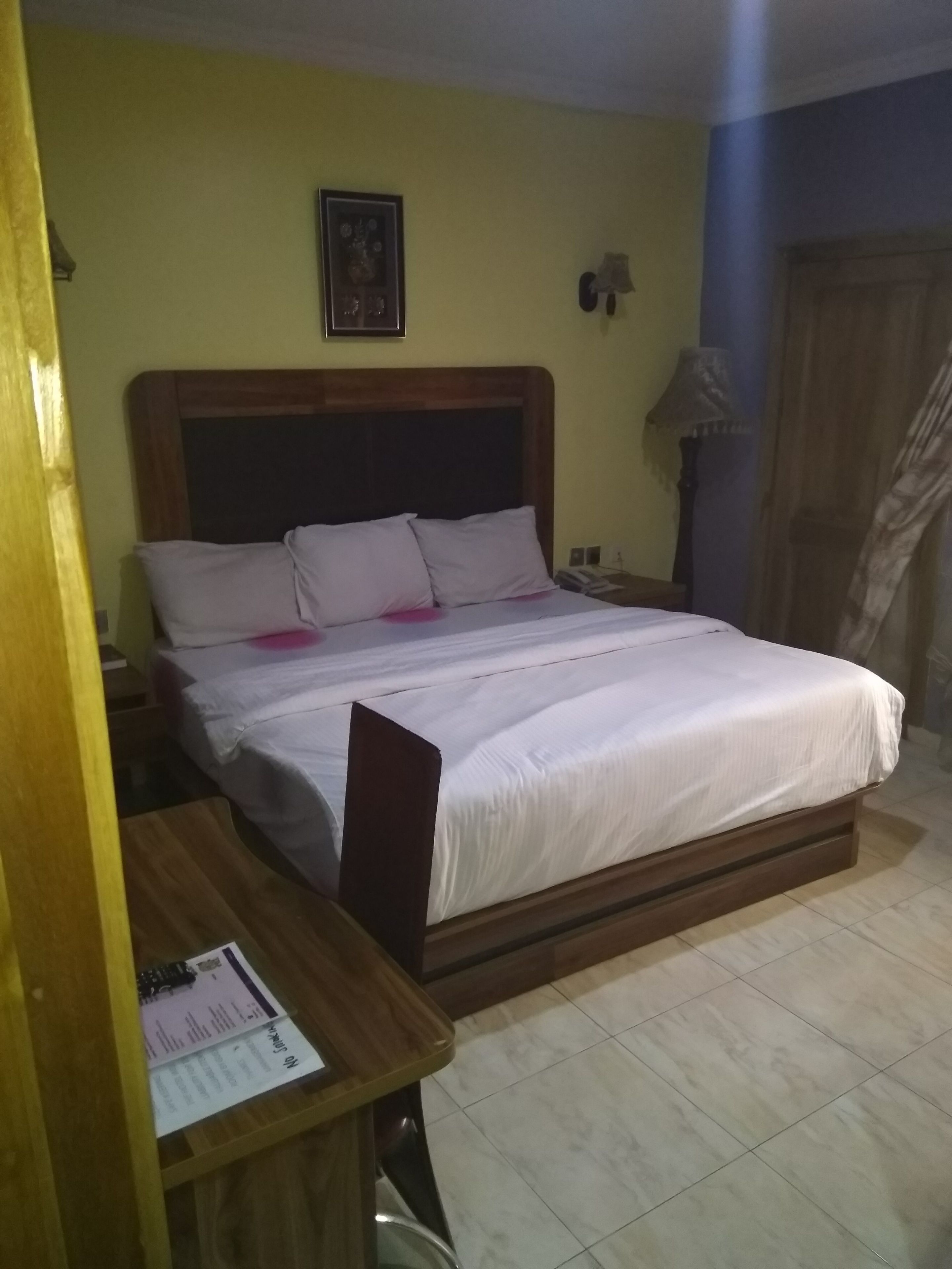 Una camera d'albergo con un letto, un comodino, una lampada e una finestra con tende.