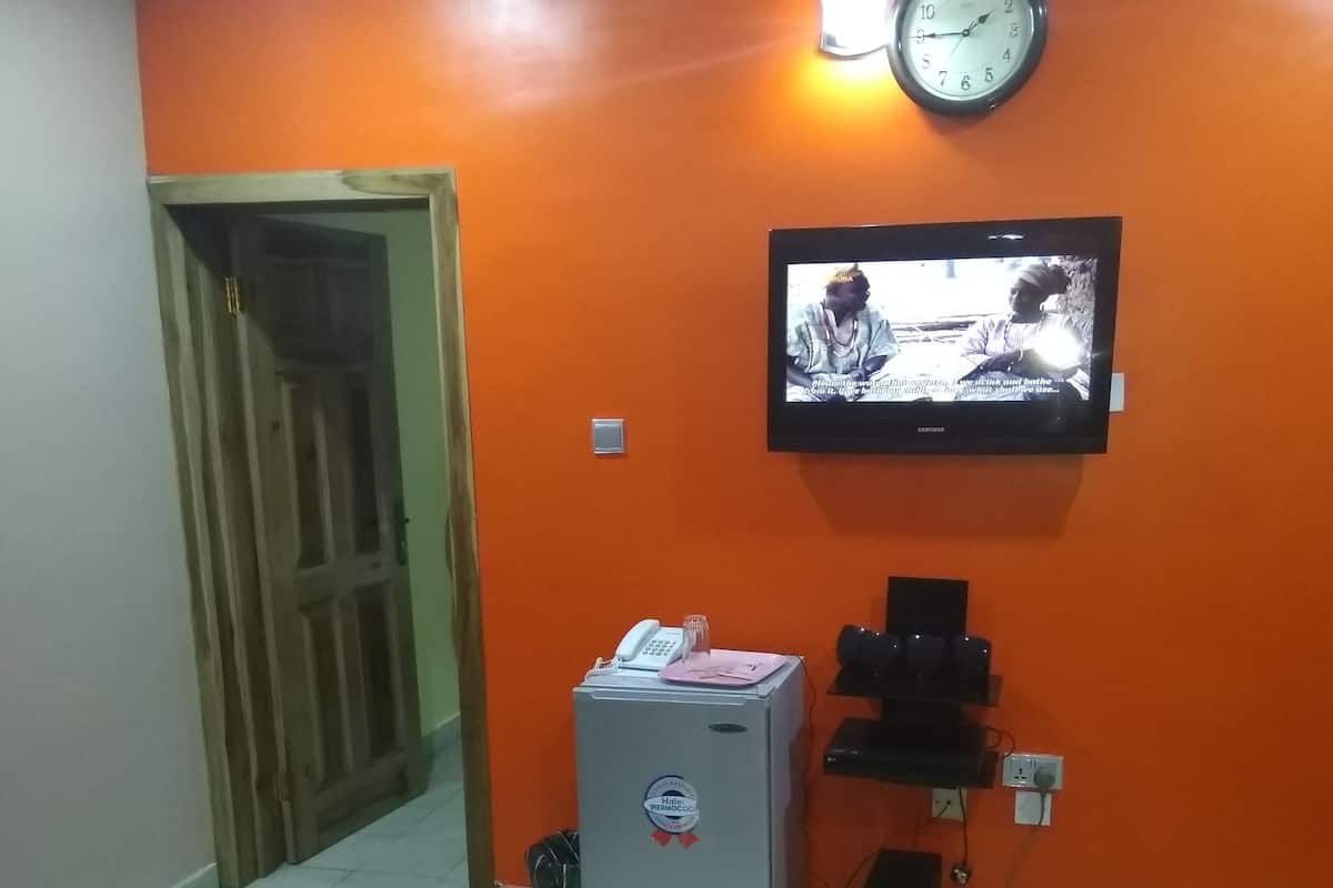 Sala de estar com parede laranja, relógio, televisão, geladeira, máquina de café e mesa com documentos.