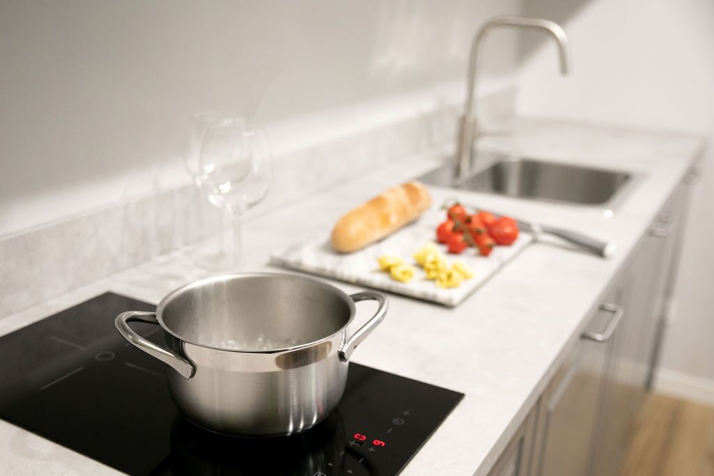 A modern kitchen with an induction cooktop, a stainless steel pot, a loaf of bread, tomatoes, and a cutting board with vegetables.