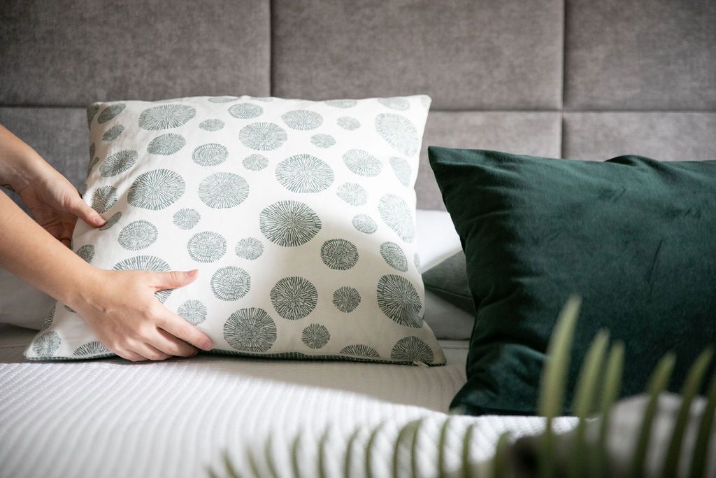 A pillow with a circular pattern on a bed with a grey headboard.