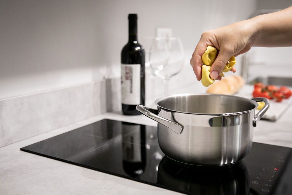 A hand holding a yellow item over a stainless steel pot on an induction cooktop.