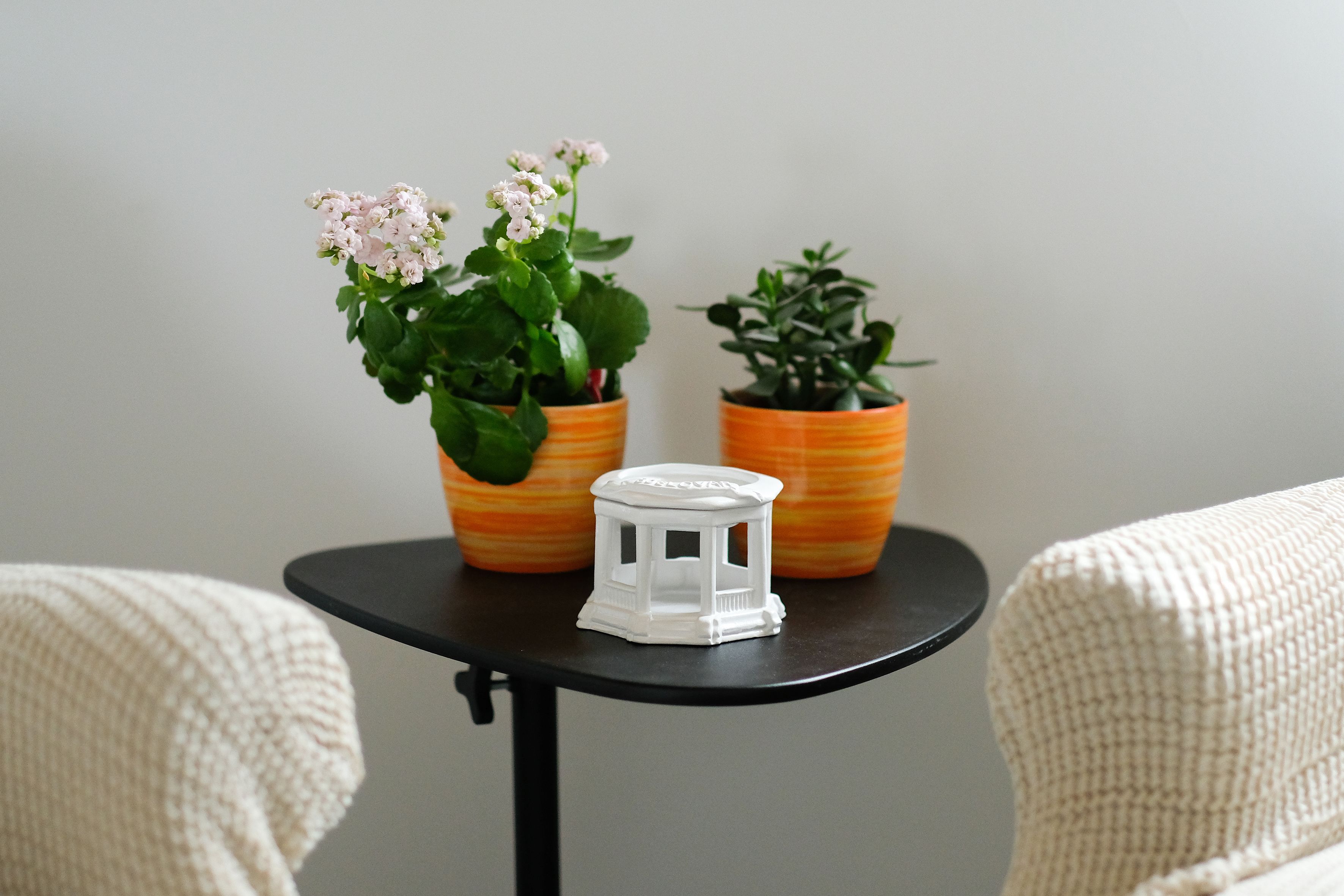 A small table with two potted plants and a white decorative item.