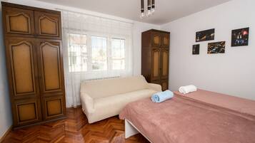 A bedroom with a bed, a sofa, wooden wardrobes, a window with curtains, and wall art.