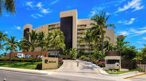 A hotel with a modern design, palm trees, and a clear blue sky. - Luxury Beachfront Condo at Del Canto Residences with Beautiful Ocean Views (Nuevo Vallarta)