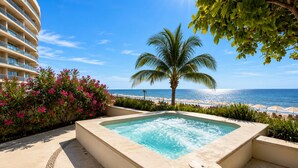 A hot tub with a view of the ocean, a palm tree, and a building with balconies. - Luxury Beachfront Condo at Del Canto Residences with Beautiful Ocean Views (Nuevo Vallarta)