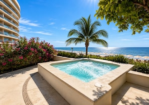 A hot tub with a view of the ocean, a palm tree, and a building with balconies.
