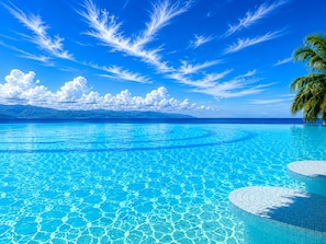 A clear blue pool with a circular design, surrounded by a tropical landscape with palm trees and distant mountains.