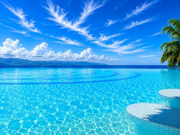 A clear blue pool with a circular design, surrounded by a tropical landscape with palm trees and distant mountains. - Luxury Beachfront Condo at Del Canto Residences with Beautiful Ocean Views (Nuevo Vallarta)
