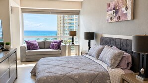 A bedroom with a large bed, a sofa, a nightstand, a lamp, and a view of the ocean. - Luxury Beachfront Condo at Del Canto Residences with Beautiful Ocean Views (Nuevo Vallarta)