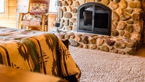 A cozy cabin interior with a stone fireplace, a mounted television, and a patterned throw blanket on the bed. - Edenwood Ranch Private SQ MILE (Wautoma)