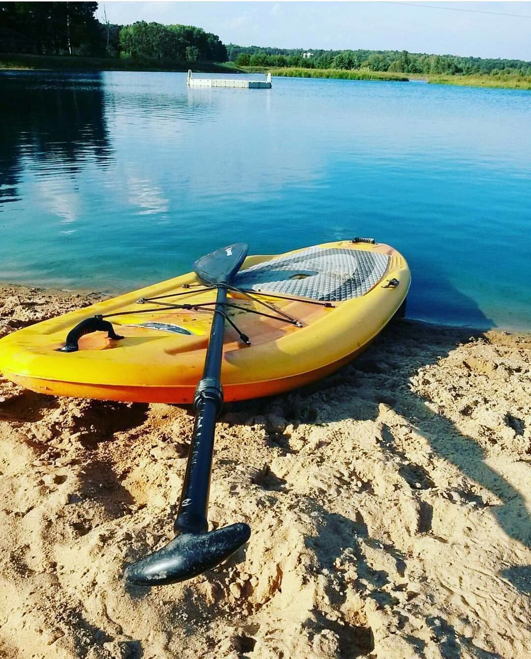 A kayak and paddle on a sandy beach by a calm lake.