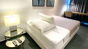Una habitación de hotel con una cama, una mesita de noche con lámpara, y dos cuadros en la pared.